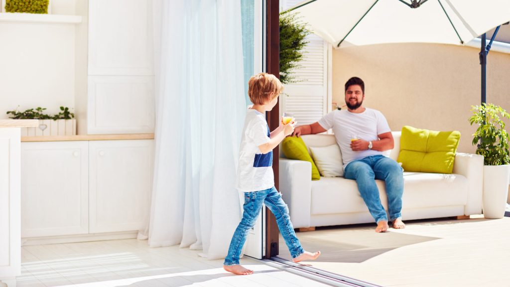 Vater und Sohn trinken Orangensaft auf sonnendurchfluteter Terasse