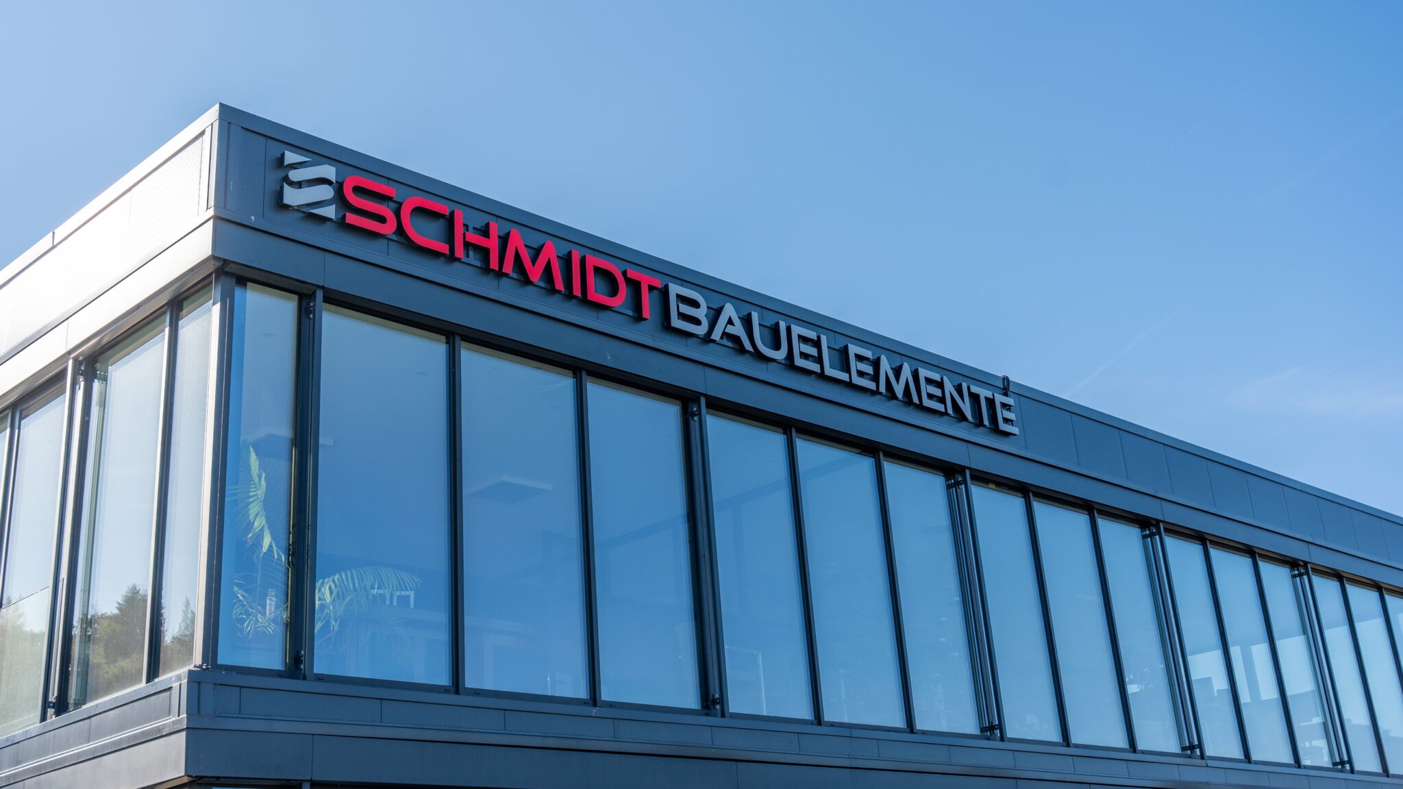 Modernes Firmengebäude von Schmidt Bauelemente mit großflächigen Glasfassaden und klarer Architektur unter blauem Himmel.